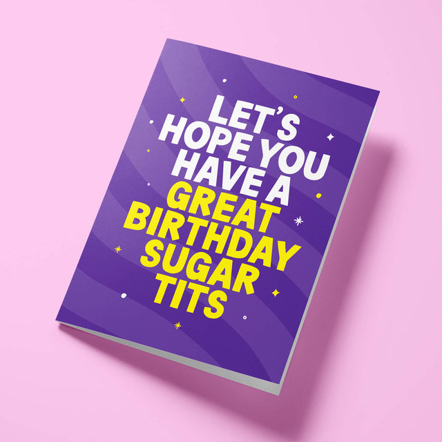 Purple 'Sugar Tits' rude birthday card laid flat at an angle on a bright background, with bright yellow 'GREAT BIRTHDAY SUGAR TITS' lettering standing out against the white text.