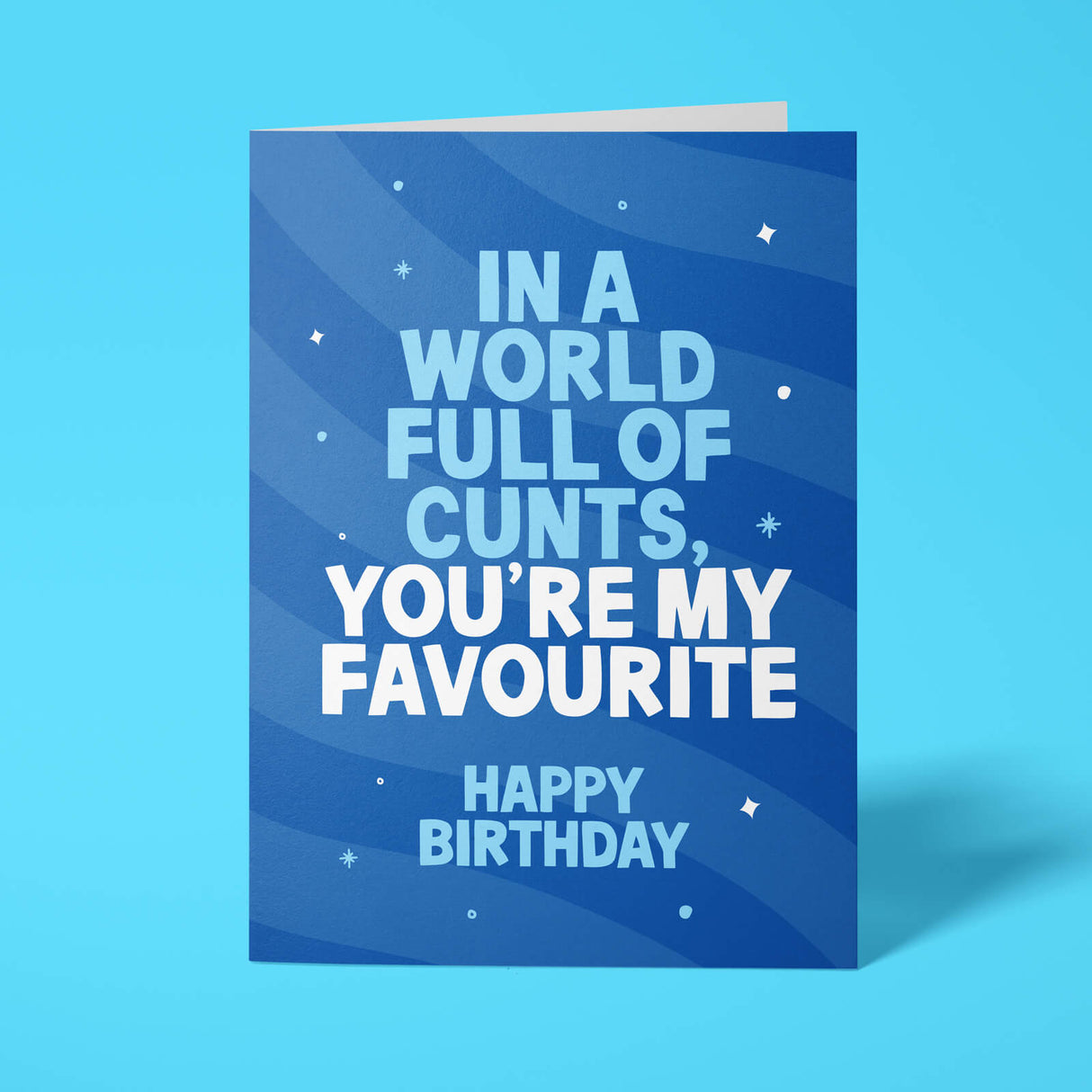 A blue birthday card with white text reading 'IN A WORLD FULL OF CUNTS, YOU'RE MY FAVOURITE HAPPY BIRTHDAY' and small white star accents, shown standing against a bright blue background.