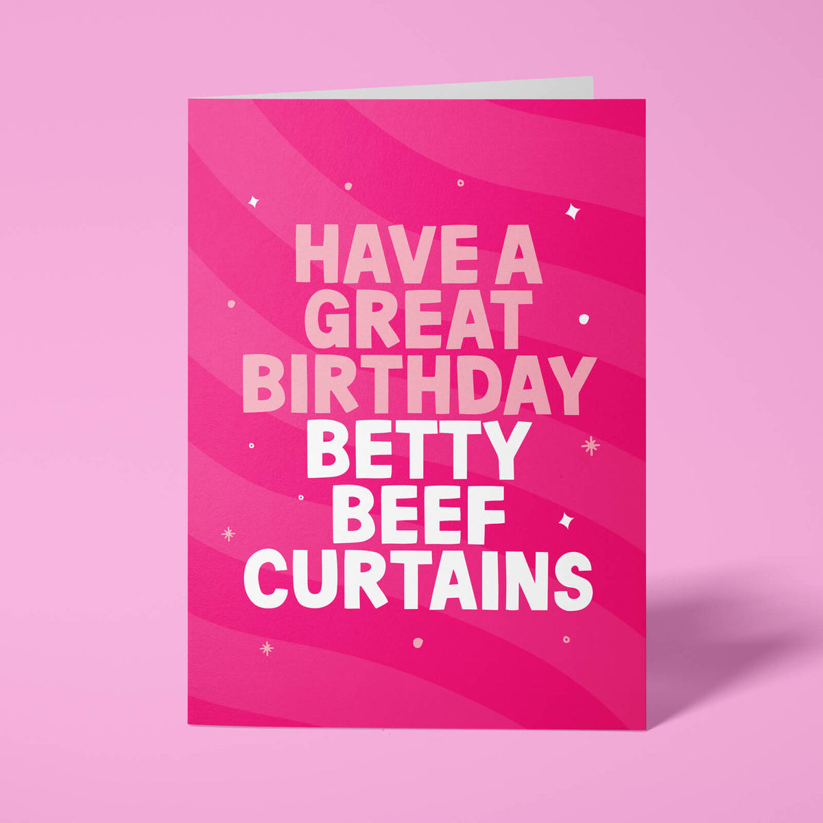 Hot pink rude birthday card standing upright against a pale pink background. Pale pink and white chunky typography reads 'HAVE A GREAT BIRTHDAY BETTY BEEF CURTAINS' over flowing pink wave stripes with white sparkle and dot details.