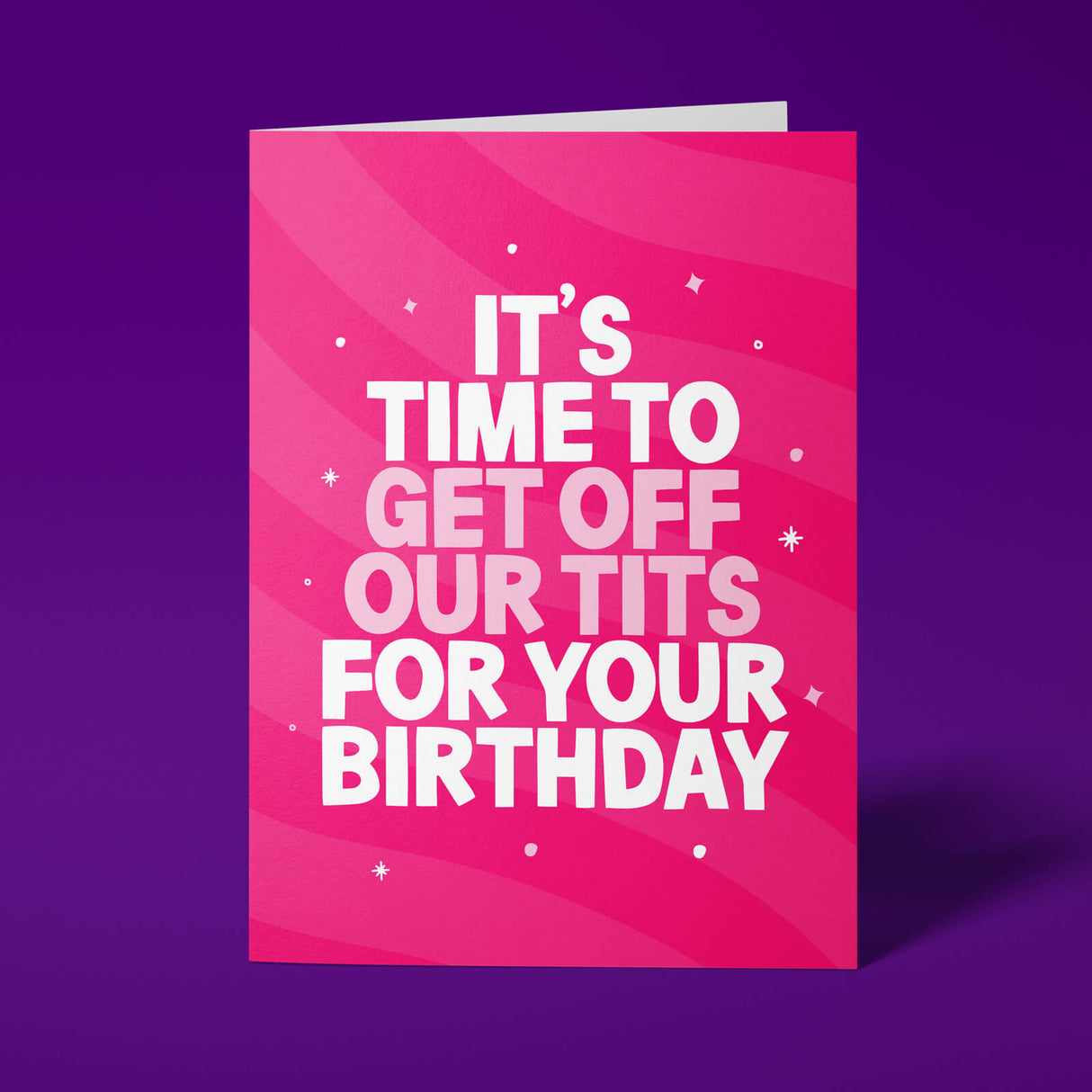 Hot pink A5 greeting card standing upright against a deep purple background. Bold white and pale pink chunky typography reads 'IT'S TIME TO GET OFF OUR TITS FOR YOUR BIRTHDAY'. Diagonal wave and swirl pattern across the card in lighter pink tones with scattered star details.