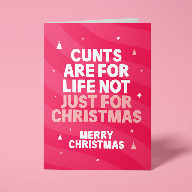 Raspberry pink rude Christmas card standing upright on a bright background. Bold white and pale pink chunky typography reads 'CUNTS ARE FOR LIFE NOT JUST FOR CHRISTMAS MERRY CHRISTMAS' over pink wave stripes with white and pale pink Christmas tree and sparkle details.