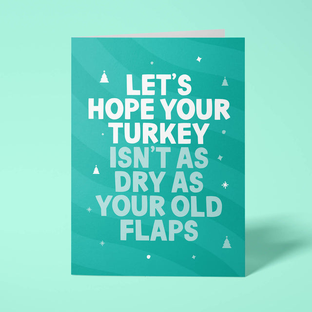 Green rude Christmas card standing upright on a bright background. Bold white and pale mint chunky typography reads 'LET'S HOPE YOUR TURKEY ISN'T AS DRY AS YOUR OLD FLAPS' over Green wave stripes with white Christmas tree and sparkle details.