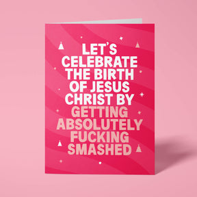 Raspberry pink rude Christmas card standing upright on a bright background. Bold white and pale pink chunky typography reads 'LET'S CELEBRATE THE BIRTH OF JESUS CHRIST BY GETTING ABSOLUTELY FUCKING SMASHED' over pink wave stripes with white and pale pink Christmas tree and sparkle details.