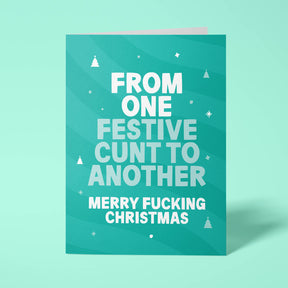 Green rude Christmas card standing upright on a bright background. Bold white and pale mint chunky typography reads 'FROM ONE FESTIVE CUNT TO ANOTHER MERRY FUCKING CHRISTMAS' over Green wave stripes with white Christmas tree and sparkle details.