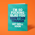 Teal rude get well soon card standing upright against a bright orange background. Bold white and dark navy chunky typography reads 'I'M SO FUCKING GLAD YOU DIDN'T DIE THOUGH GET WELL SOON' over soft teal wave stripes with yellow and navy sparkle and dot details.