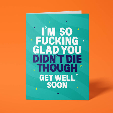 Teal rude get well soon card standing upright against a bright orange background. Bold white and dark navy chunky typography reads 'I'M SO FUCKING GLAD YOU DIDN'T DIE THOUGH GET WELL SOON' over soft teal wave stripes with yellow and navy sparkle and dot details.