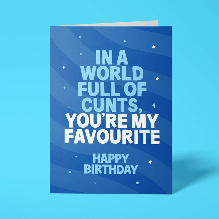 A blue birthday card with white text reading 'IN A WORLD FULL OF CUNTS, YOU'RE MY FAVOURITE HAPPY BIRTHDAY' and small white star accents, shown standing against a bright blue background.