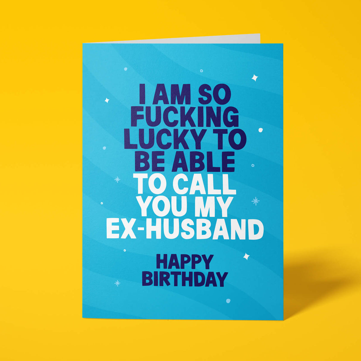 A blue greeting card with bold text reading 'I AM SO FUCKING LUCKY TO BE ABLE TO CALL YOU MY EX-HUSBAND HAPPY BIRTHDAY' on a bright yellow background.