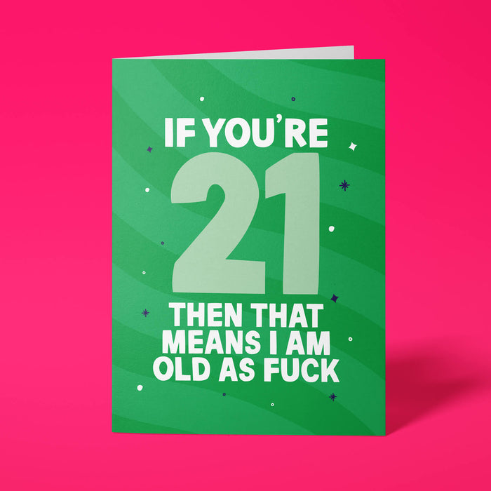 Green rude 21st birthday card standing upright on a bright pink background. White and pale mint chunky typography reads ‘IF YOU’RE 21 THEN THAT MEANS I AM OLD AS FUCK’ over green wave stripes with navy and white sparkle details.