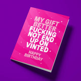 A pink birthday card with bold white text reading 'MY GIFT BETTER FUCKING NOT END UP ON VINTED' and 'HAPPY BIRTHDAY' underneath, shown at an angle on a solid purple background.