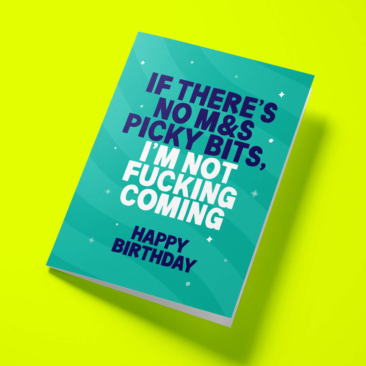 A teal greeting card with bold text reading 'IF THERE'S NO M&S PICKY BITS, I'M NOT FUCKING COMING' and 'HAPPY BIRTHDAY' in white and dark blue, shown at an angle on a bright yellow background.