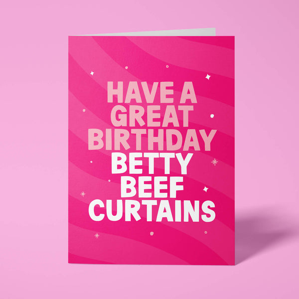 Hot pink rude birthday card standing upright against a pale pink background. Pale pink and white chunky typography reads 'HAVE A GREAT BIRTHDAY BETTY BEEF CURTAINS' over flowing pink wave stripes with white sparkle and dot details.