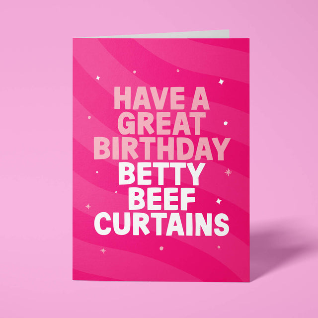 Hot pink rude birthday card standing upright against a pale pink background. Pale pink and white chunky typography reads 'HAVE A GREAT BIRTHDAY BETTY BEEF CURTAINS' over flowing pink wave stripes with white sparkle and dot details.