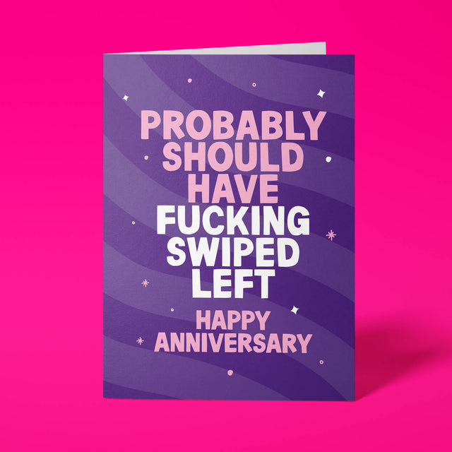 Deep purple anniversary card with pink and white block-capital text reading "PROBABLY SHOULD HAVE FUCKING SWIPED LEFT, HAPPY ANNIVERSARY," decorated with hand-drawn stars, dots and sparkle icons.