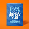 Royal blue anniversary card with pale blue and white block-capital text reading "YOU'RE SUCH A LUCKY FUCKER YOU, HAPPY ANNIVERSARY," decorated with hand-drawn stars, dots and sparkle icons.