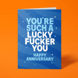 Royal blue anniversary card with pale blue and white block-capital text reading "YOU'RE SUCH A LUCKY FUCKER YOU, HAPPY ANNIVERSARY," decorated with hand-drawn stars, dots and sparkle icons.